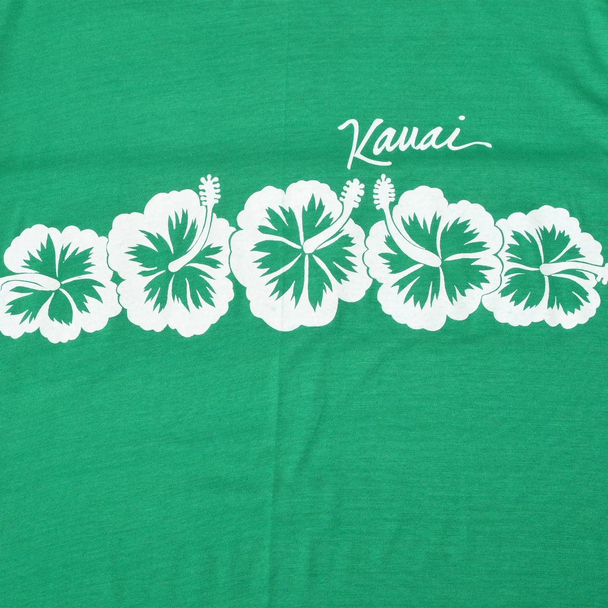 Close-up of white Kauai script and hibiscus flower print on green T-shirt