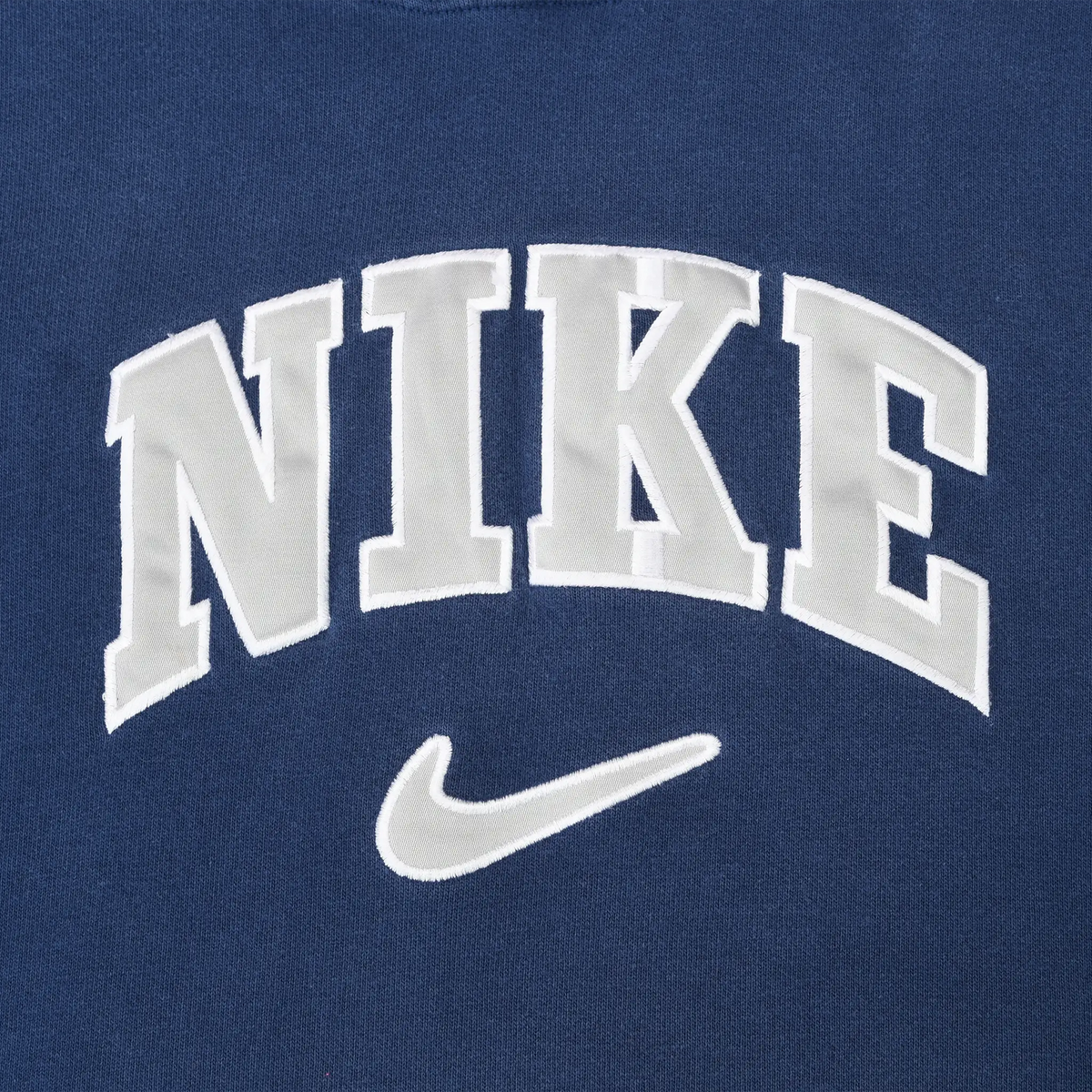 Close-up of gray Nike spellout and Swoosh embroidery on navy blue fabric