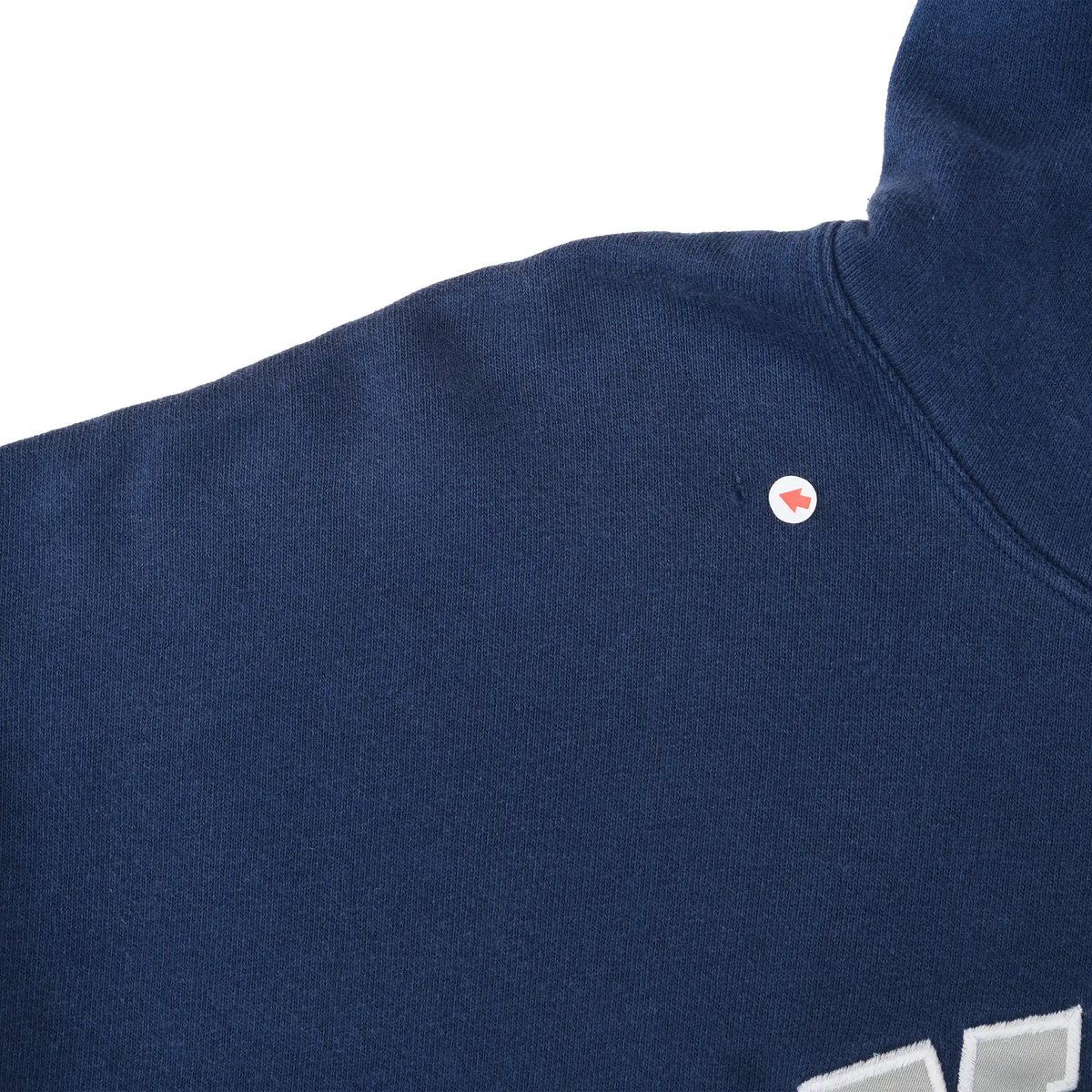 Close-up of a small red and white mark near the shoulder of the navy blue hoodie
