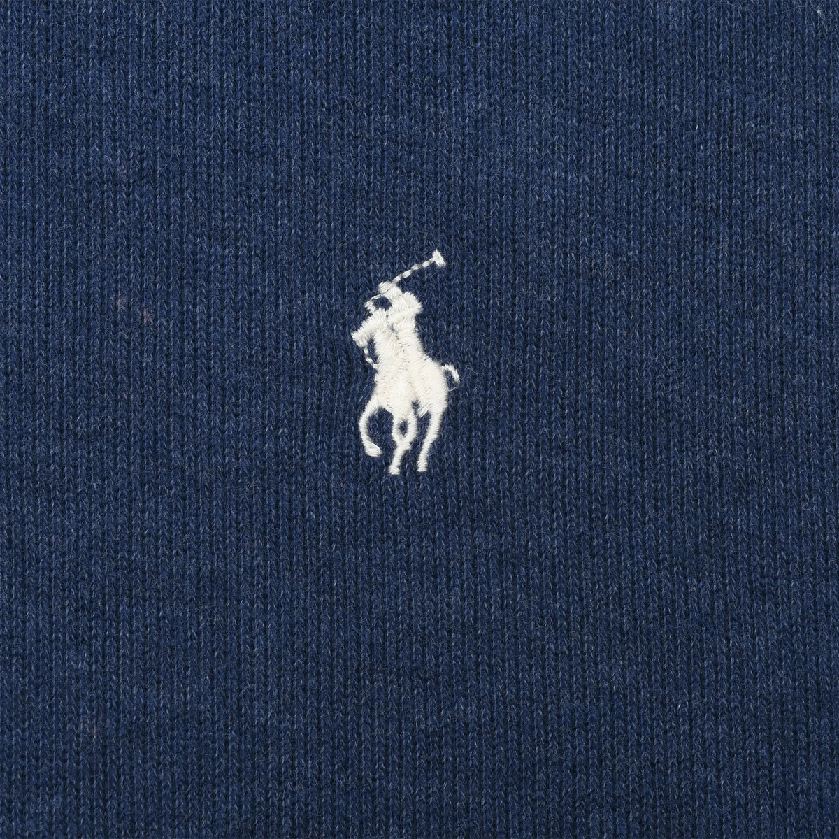 Close-up of white Polo pony embroidery on blue sweater fabric