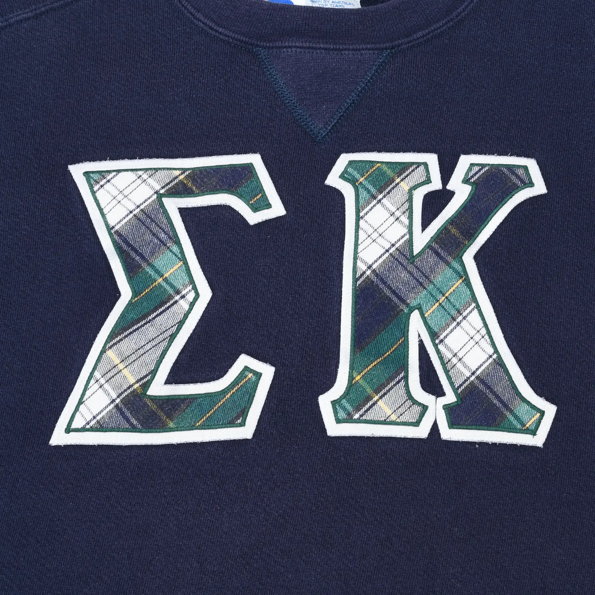 Close-up of plaid Epsilon Kappa letter appliqué on navy sweatshirt