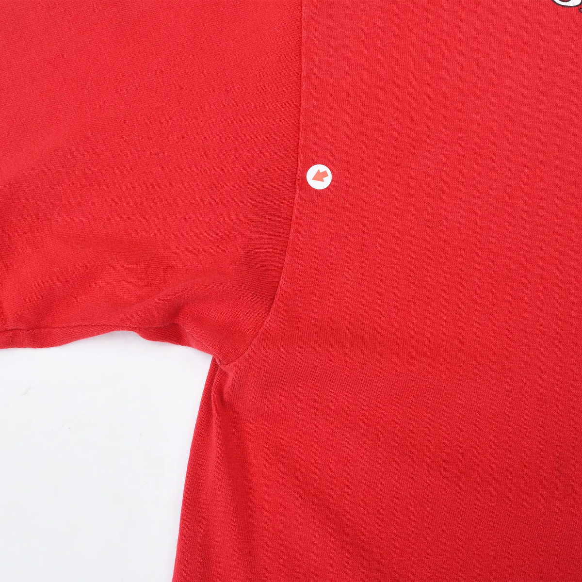 Close-up of red T-shirt underarm seam with a small hole marked by an arrow