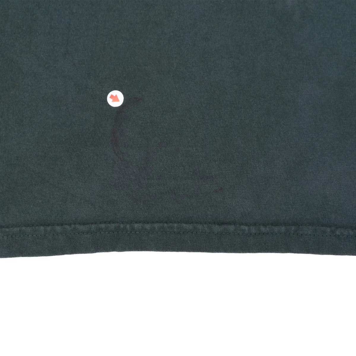 Close-up of lower T-shirt hem with marker indicating a small reddish spot