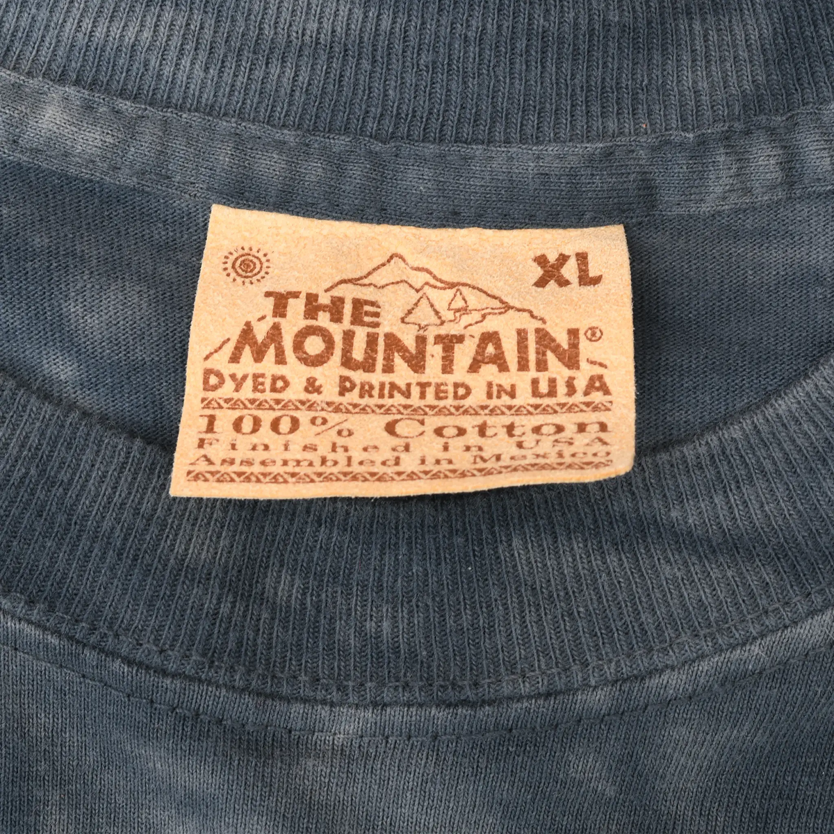 Close-up of The Mountain neck label marked XL, 100% cotton, dyed and printed in USA