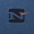 Close-up of black Nike emblem and orange Swoosh embroidery on blue fabric