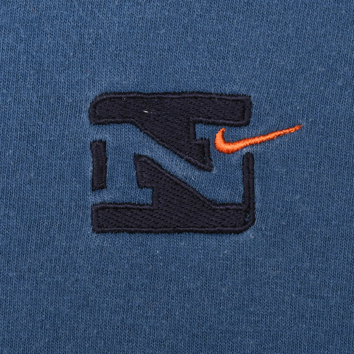 Close-up of black Nike emblem and orange Swoosh embroidery on blue fabric