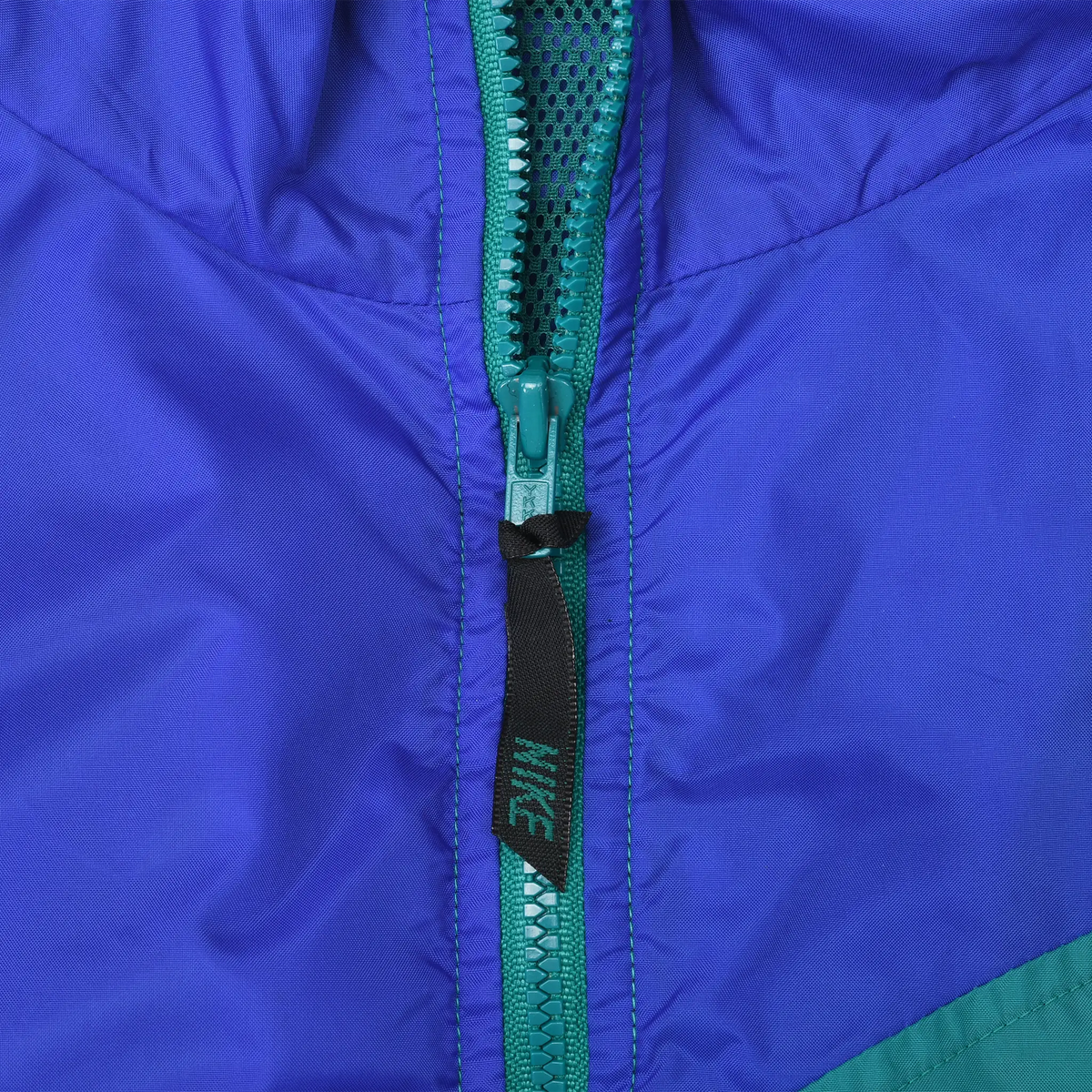 Close-up of teal front zipper and Nike-branded pull tab on blue fabric
