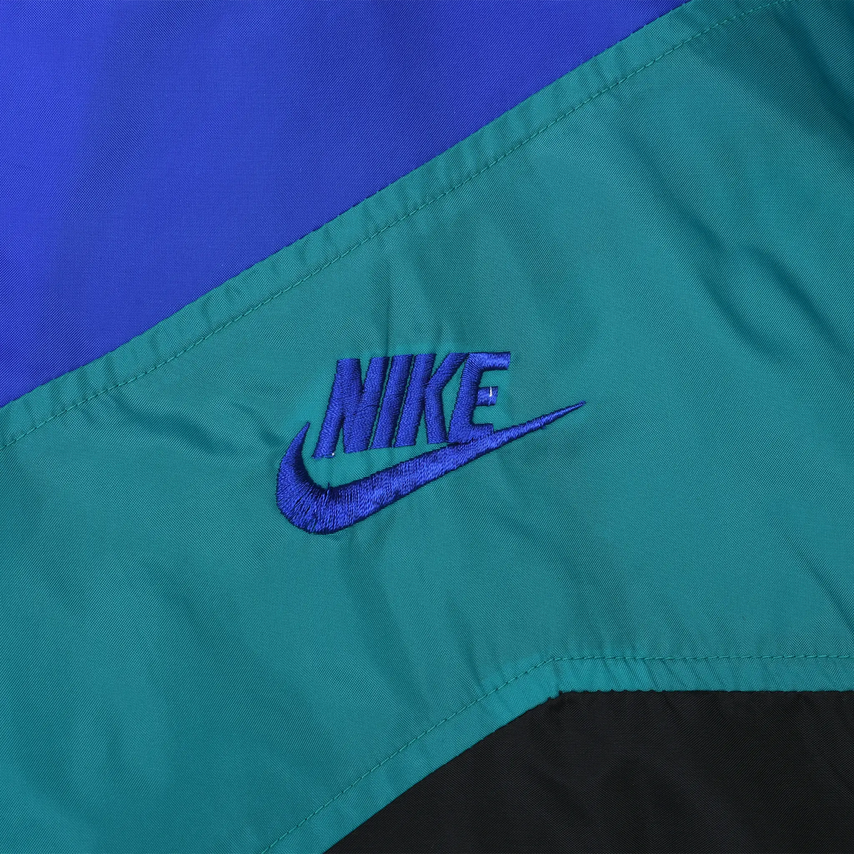 Close-up of blue Nike Swoosh embroidery on the teal chest panel