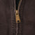 Close-up of brass-tone Carhartt zipper pull on brown jacket fabric