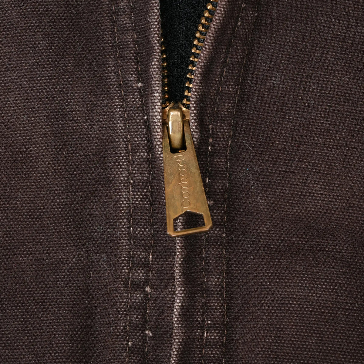 Close-up of brass-tone Carhartt zipper pull on brown jacket fabric