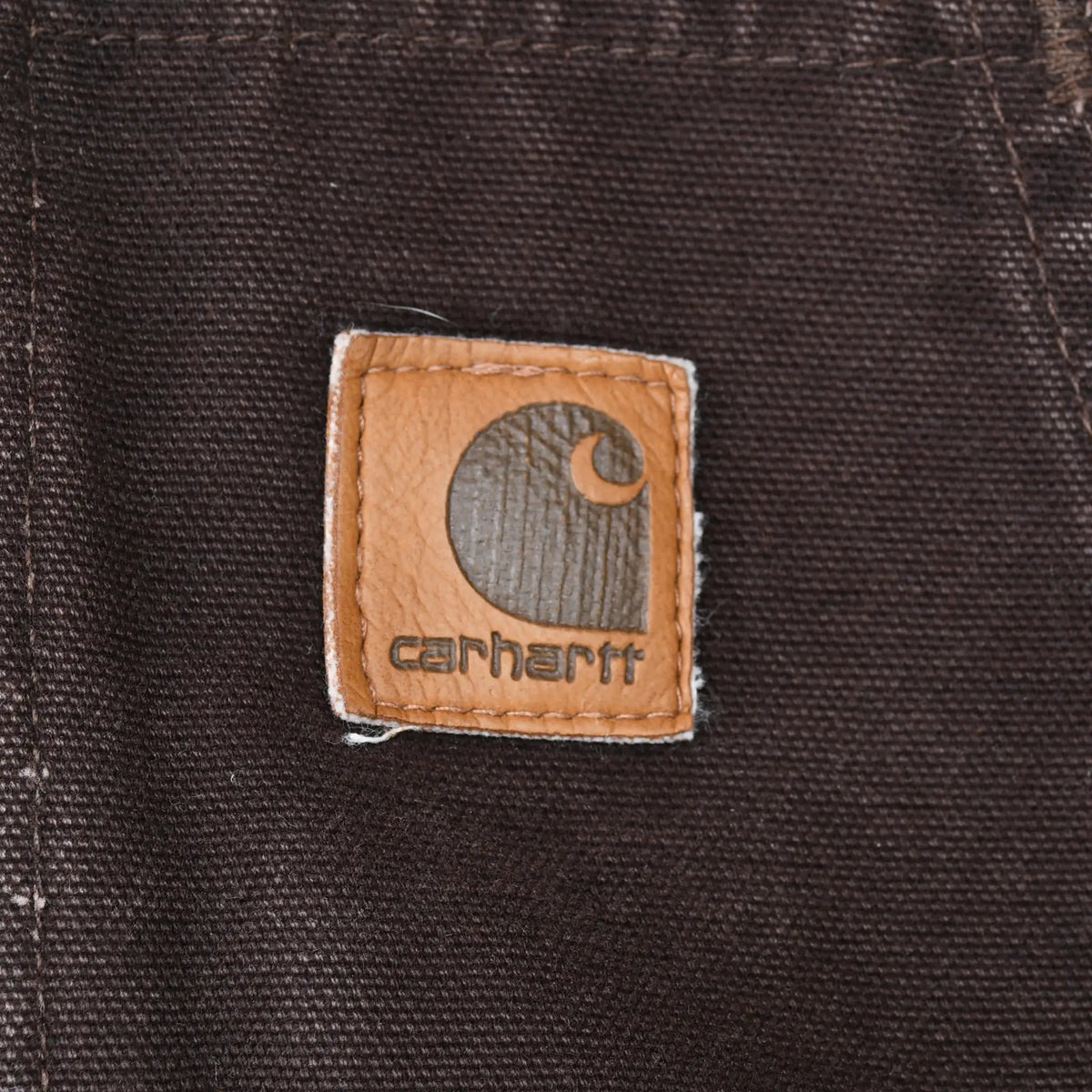 Close-up of square Carhartt logo patch stitched to brown jacket pocket