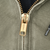 Close-up of gold-tone Carhartt zipper pull on green jacket fabric