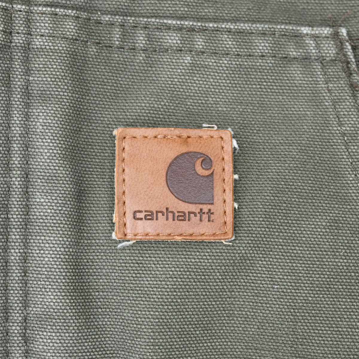 Close-up of brown Carhartt logo patch stitched onto green front pocket