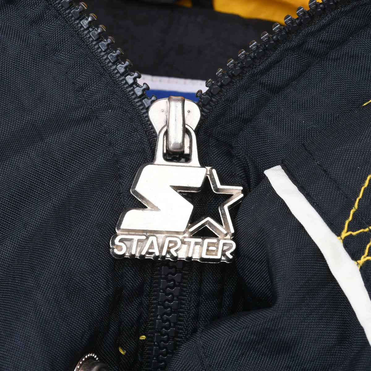 Close-up of silver Starter star logo zipper pull on the black jacket