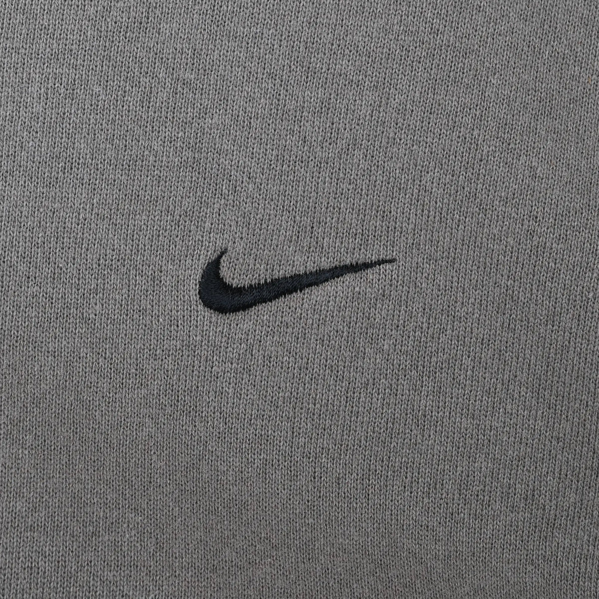 Close-up of small black Nike Swoosh embroidery on khaki sweatshirt chest