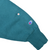 Teal sweatshirt sleeve detail with embroidered Champion logo near the ribbed cuff