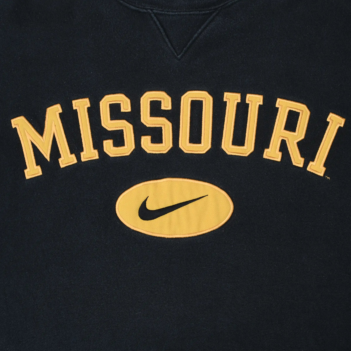 Close-up of gold Missouri lettering and Nike Swoosh chest graphic on black sweatshirt