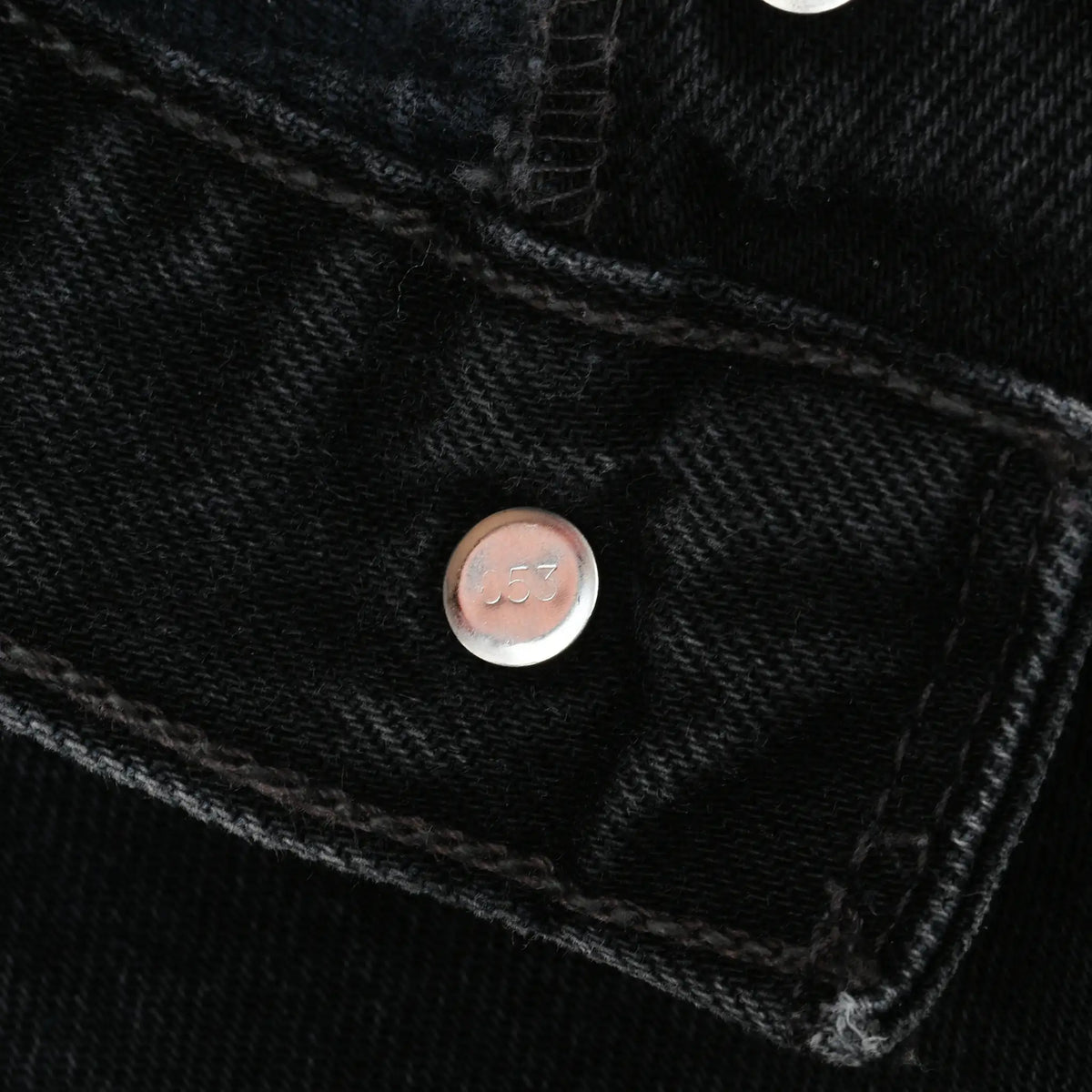 Close-up of metal button stamped 653 on black Levi's jeans