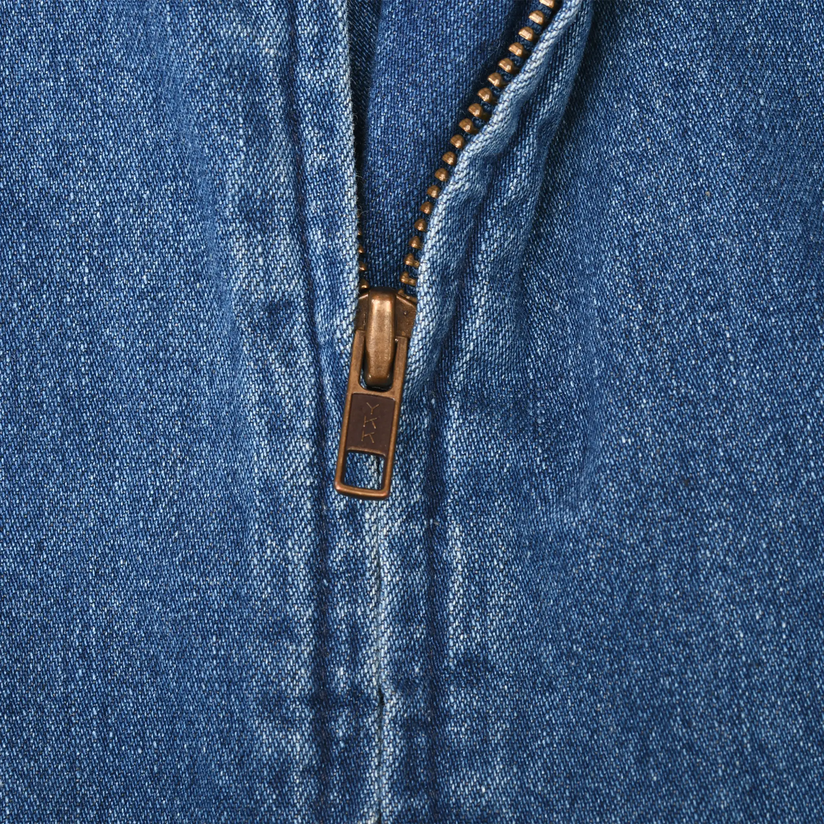 Close-up of brass-tone YKK front zipper on blue denim jacket