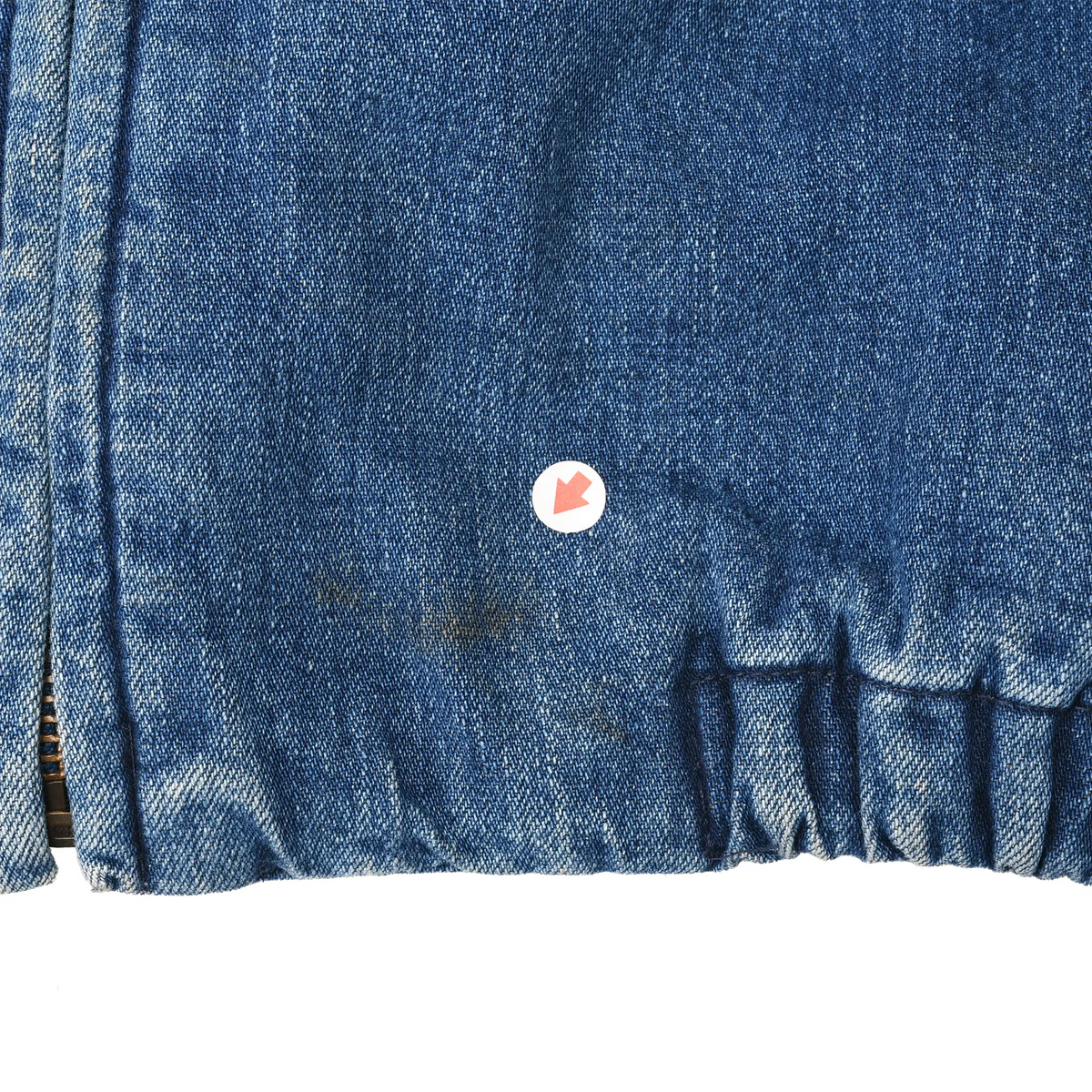 Close-up of small discolored spot near the elasticated hem of blue denim jacket