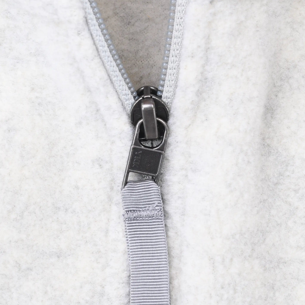 Close-up of gray zipper pull and webbing tab on beige fleece