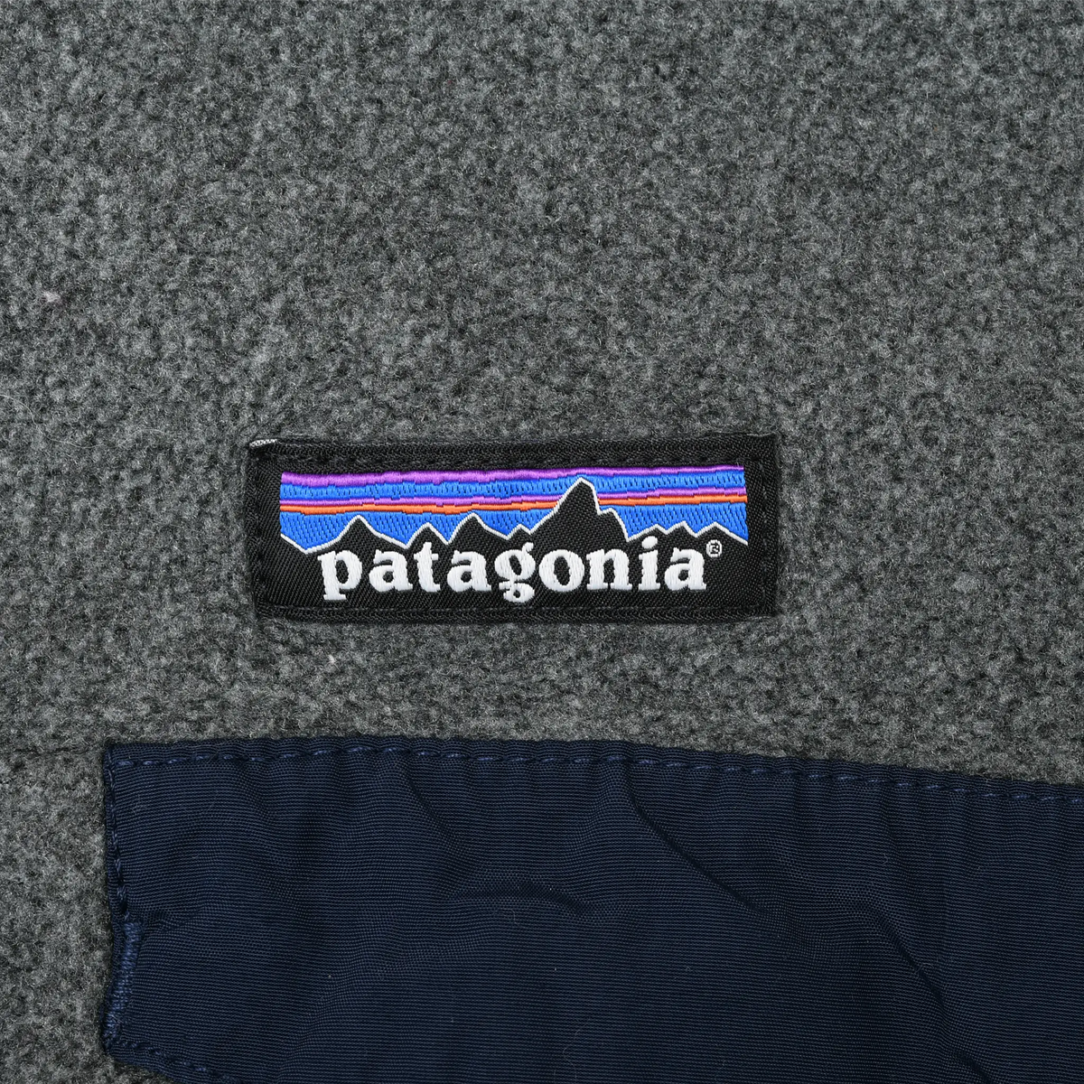 Close-up of Patagonia logo patch above the navy chest pocket flap on grey fleece