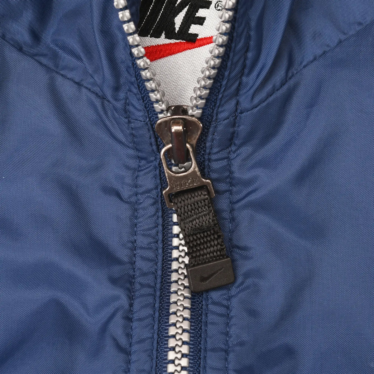 Close-up of front zipper pull and navy fabric below the Nike neck label