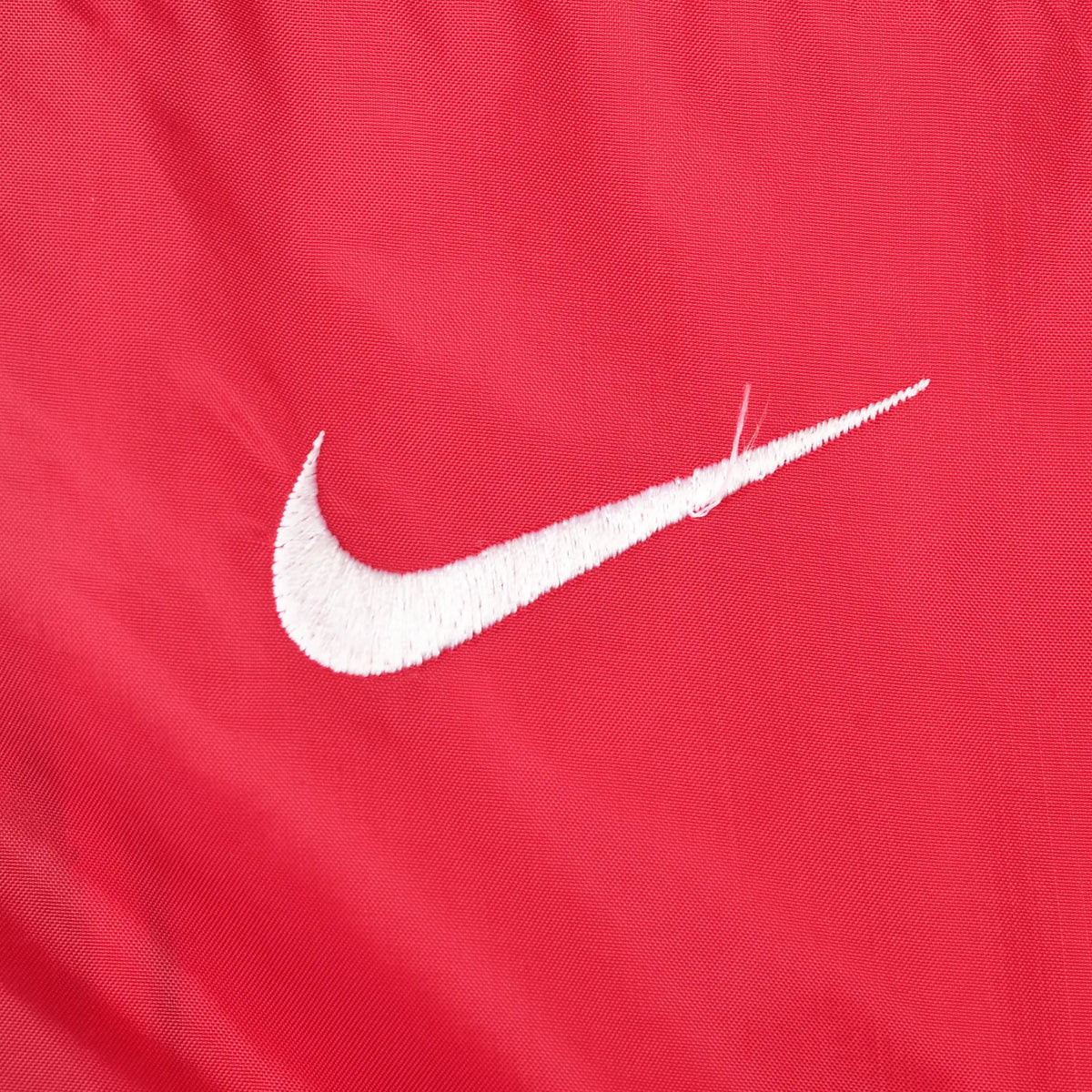 Close-up of white Nike Swoosh embroidery on the red chest panel