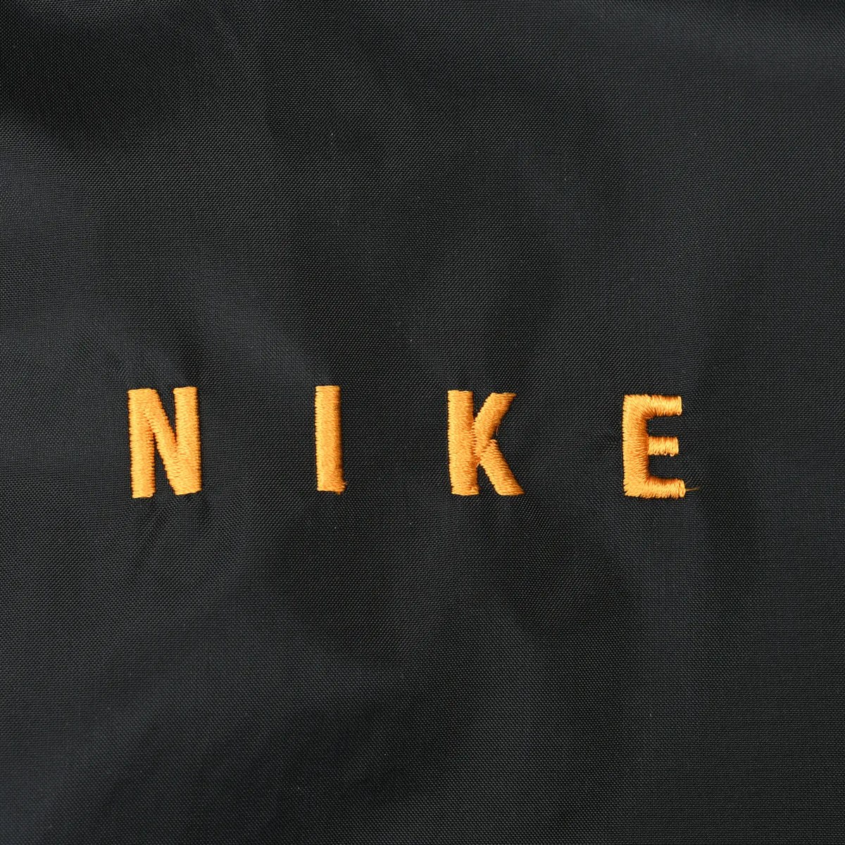 Close-up of orange NIKE embroidery on black jacket fabric