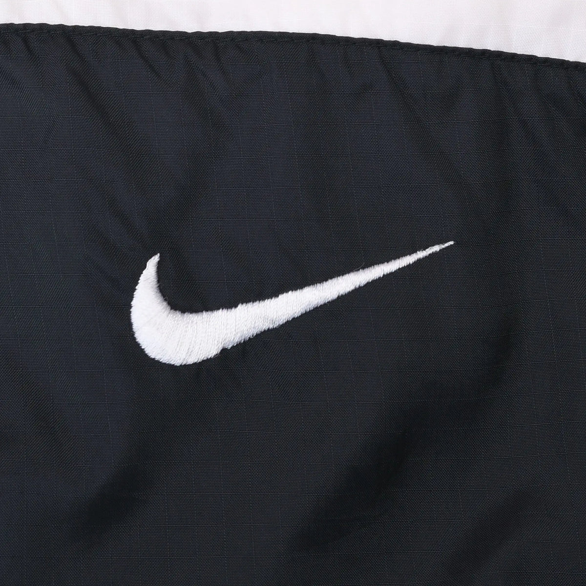 Close-up of white Nike Swoosh embroidery on black fabric