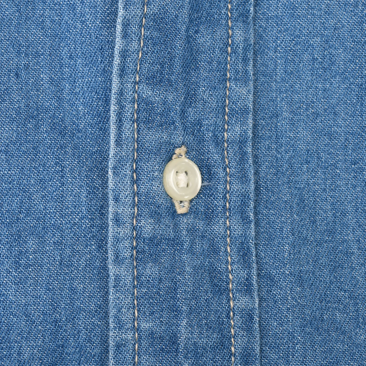Close-up of white button, buttonhole, and stitching on blue denim shirt placket