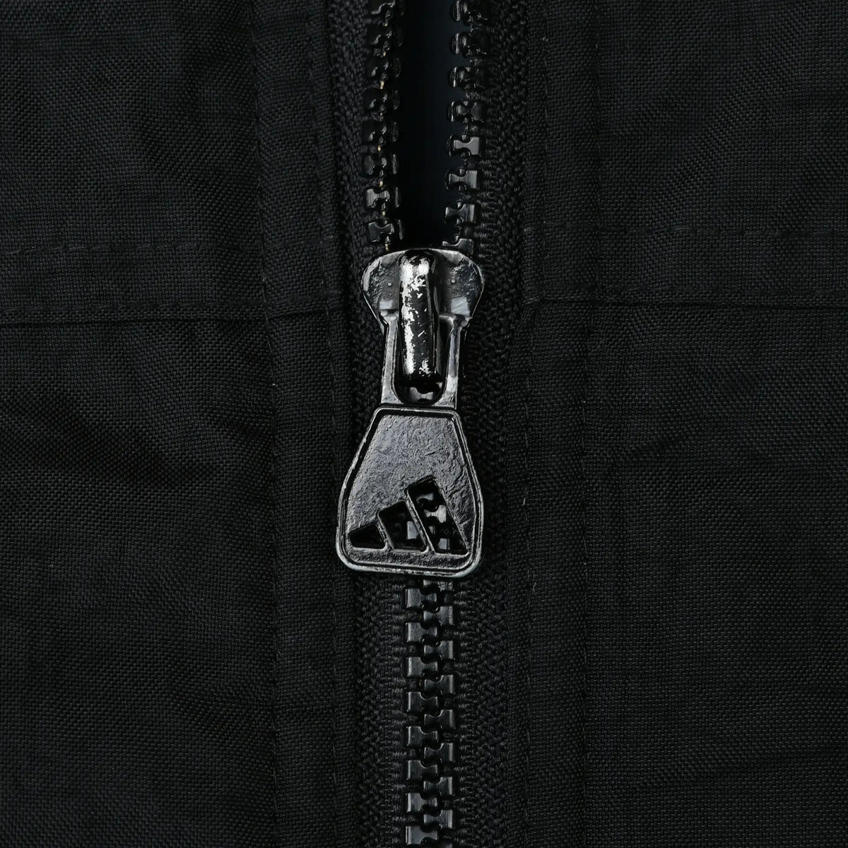 Close-up of black front zipper with Adidas logo on the metal pull