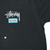 Close-up of left chest Stüssy logo and fish graphic on black T-shirt