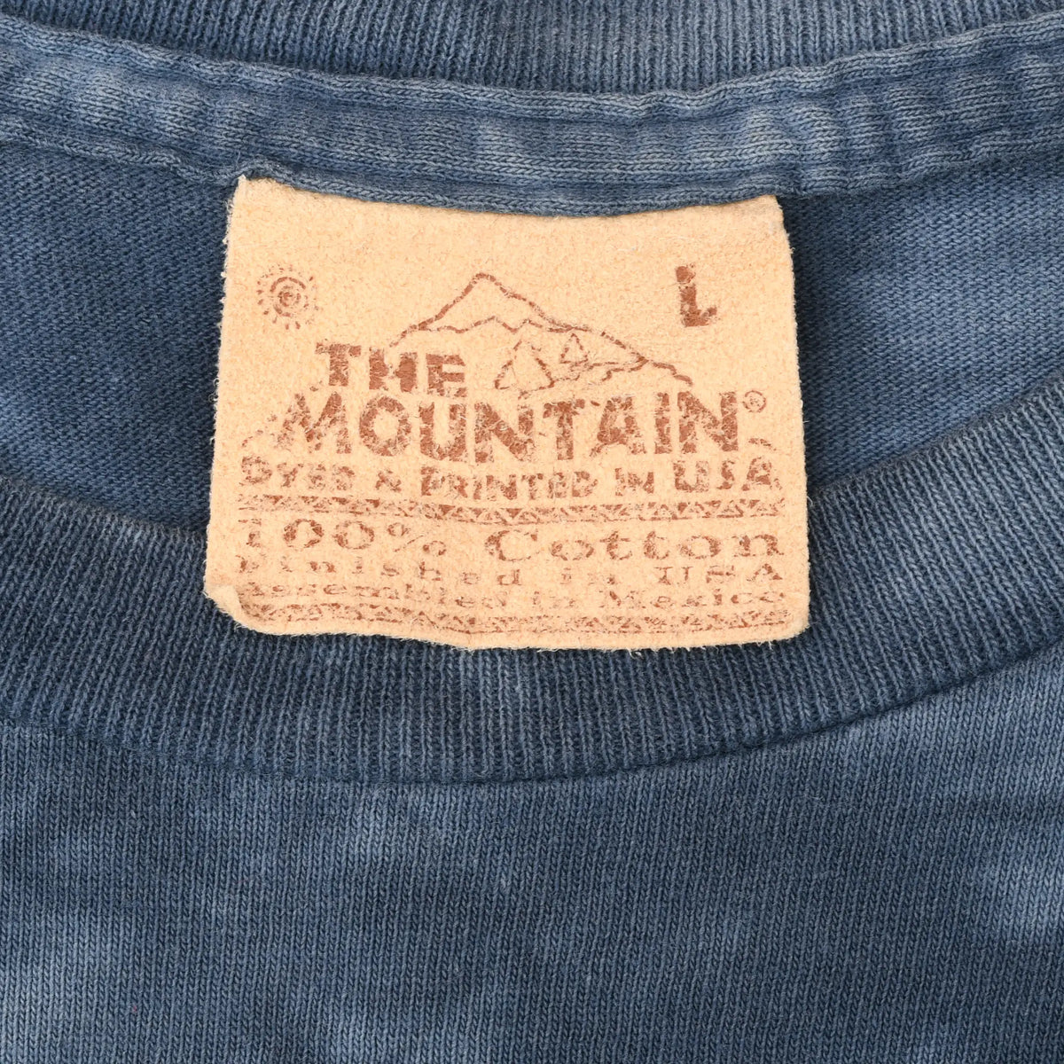 Close-up of The Mountain neck label marked L on blue T-shirt