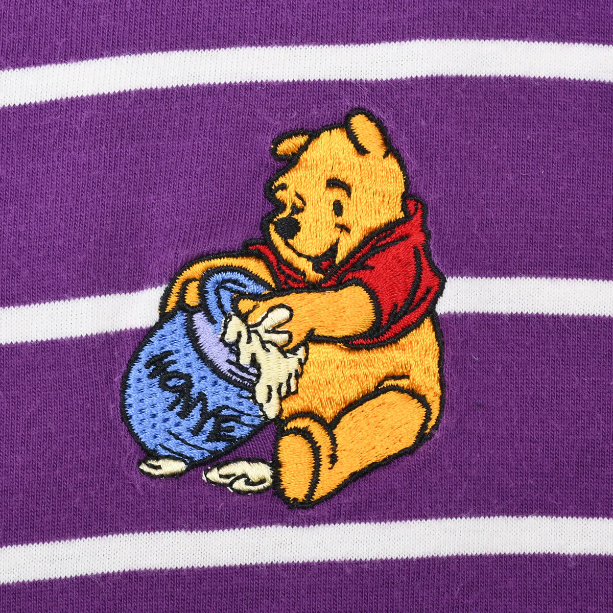 Close-up of embroidered Winnie the Pooh holding a blue honey pot on purple striped fabric