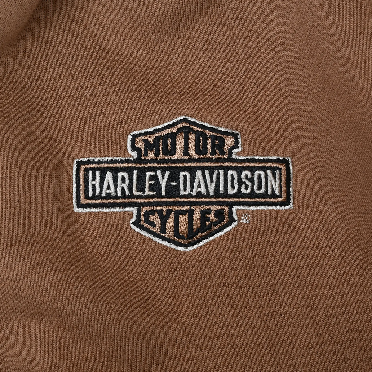 Close-up of embroidered Harley-Davidson bar-and-shield logo on brown hoodie chest