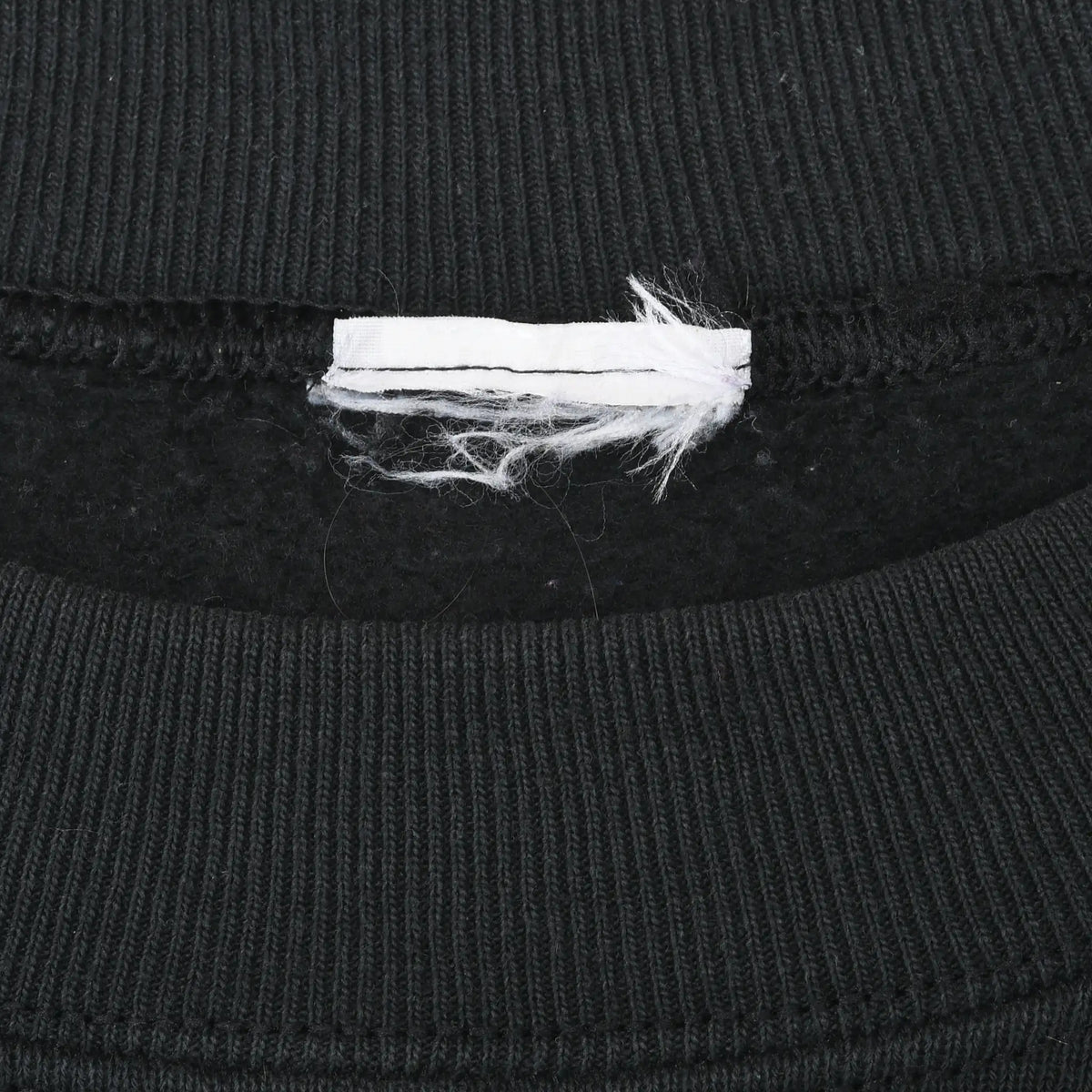 Close-up of black ribbed crewneck collar with a frayed blank white tag