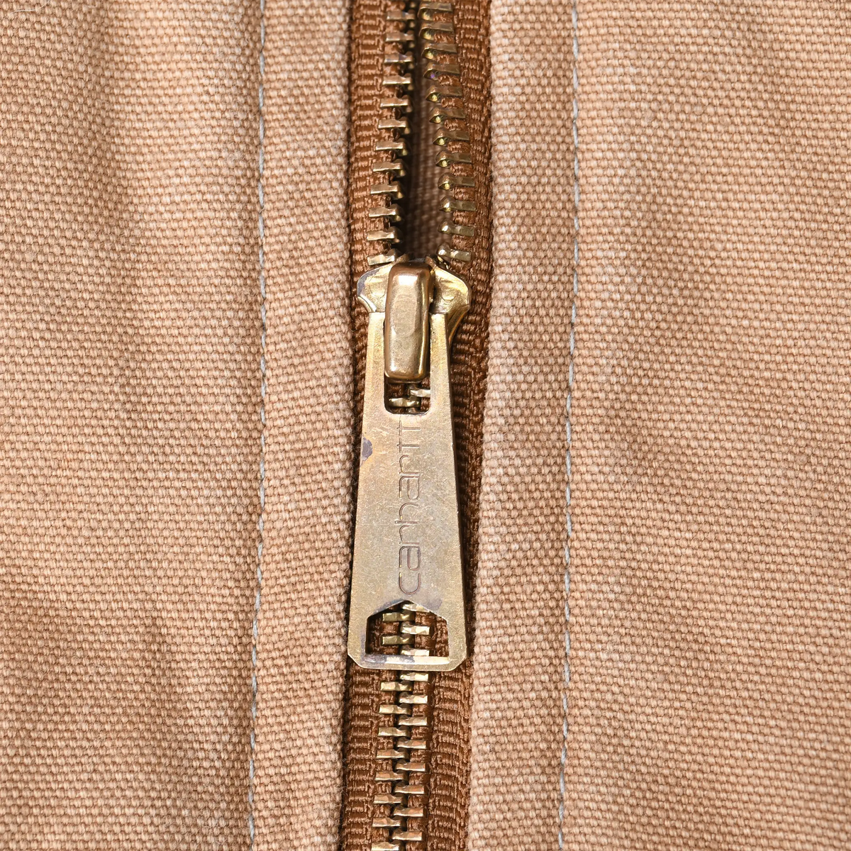 Close-up of Carhartt-engraved brass zipper pull on brown canvas vest