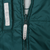 Close-up of green front zipper, grey pull tab, and care symbol label