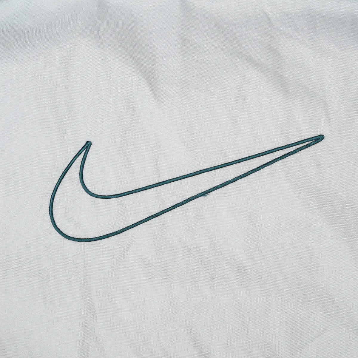 Close-up of large green outlined Nike Swoosh embroidery on light grey fabric