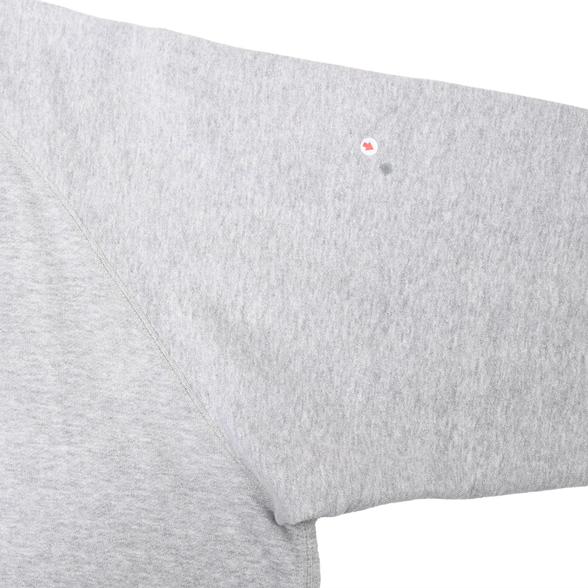 Close-up of small dark spot on grey sweatshirt sleeve, marked by an arrow