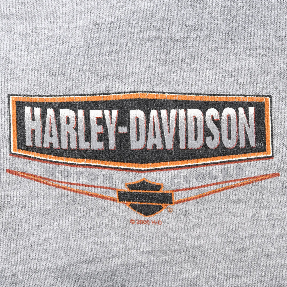 Close-up of black, orange, and white Harley-Davidson chest graphic on gray fabric