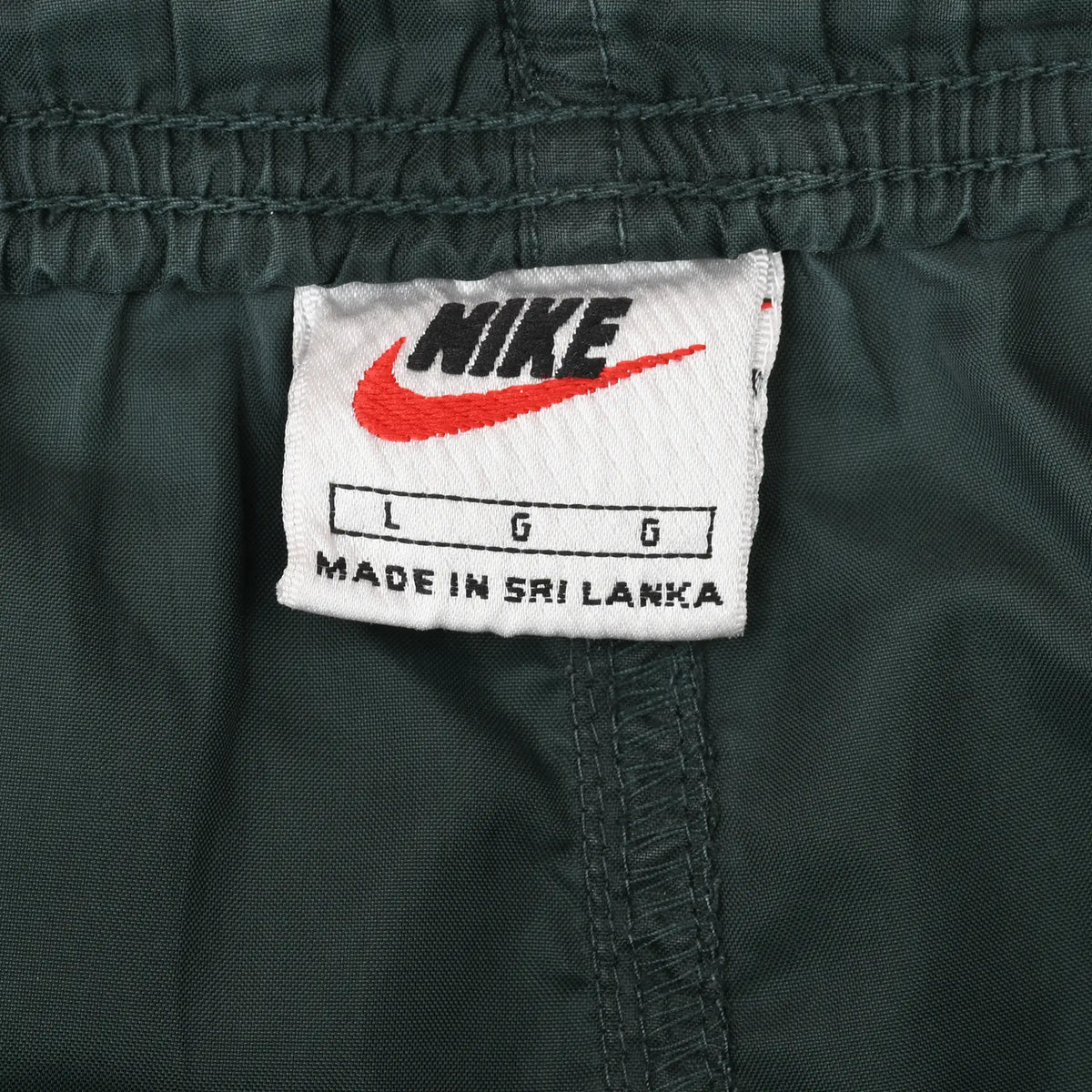 Nike waist label with red Swoosh and large size marking inside dark green track pants