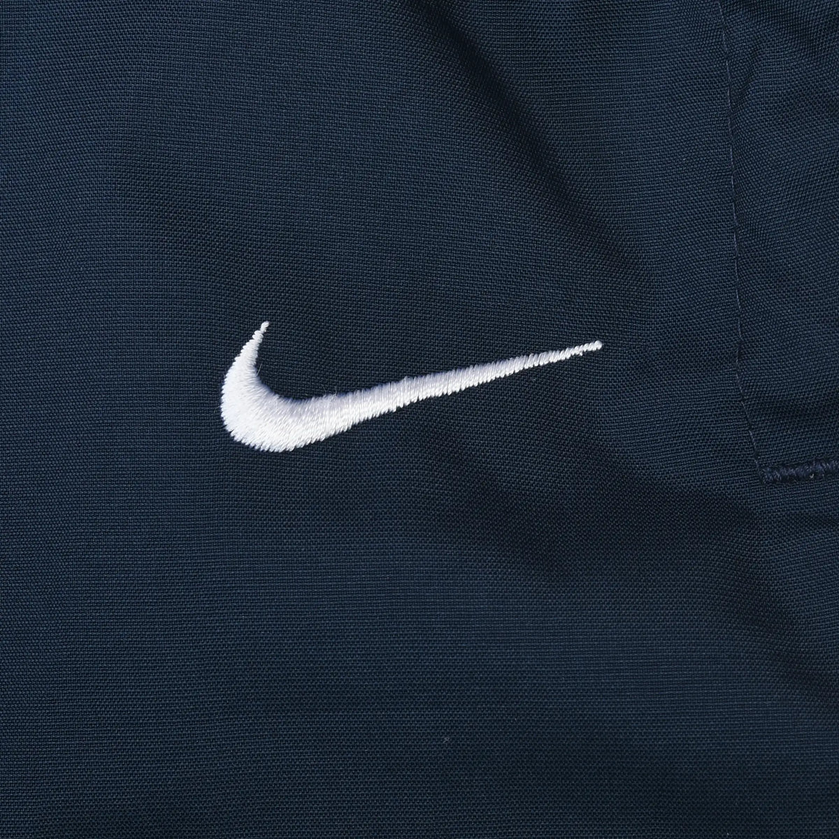 Close-up of white embroidered Nike Swoosh on blue track pants