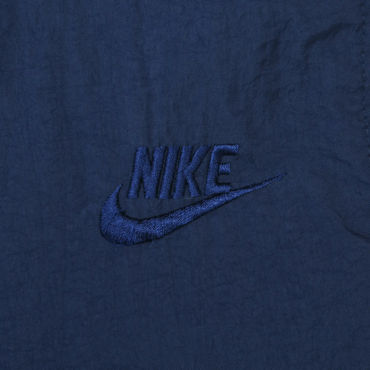 Close-up of tonal blue Nike Swoosh embroidery on navy track pants