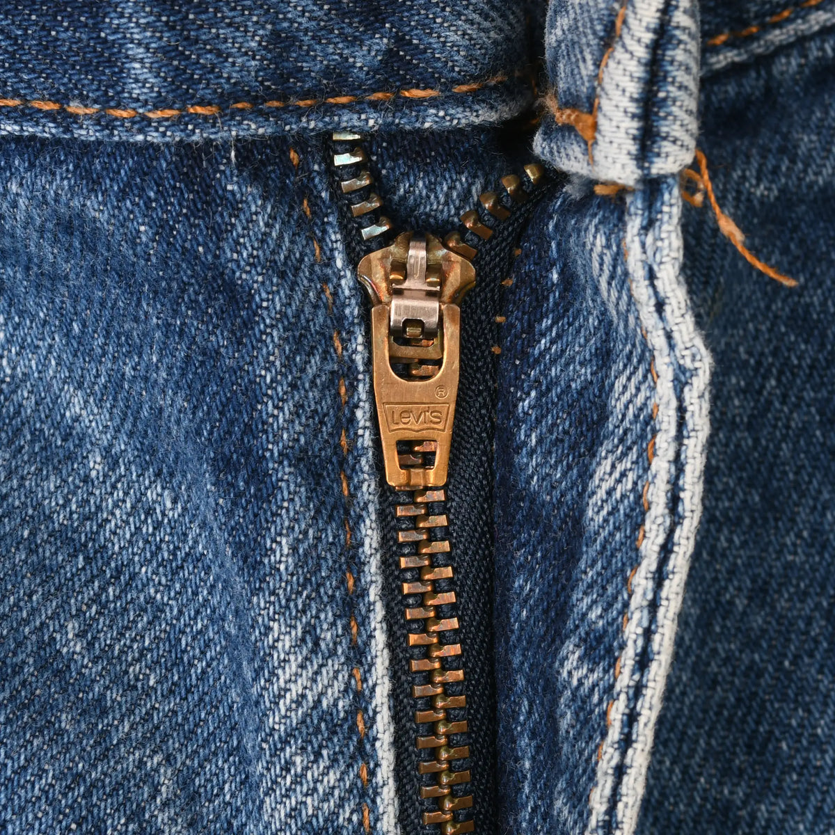 Close-up of brass Levi's zipper fly and orange stitching on blue denim