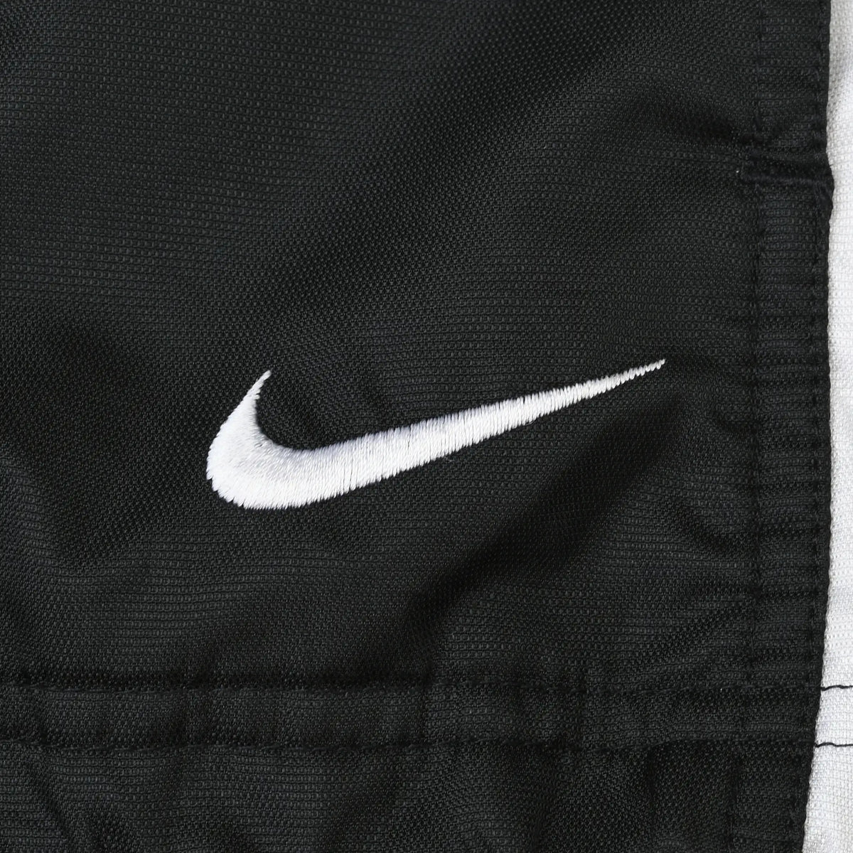 Close-up of white Nike Swoosh embroidery on black windbreaker fabric