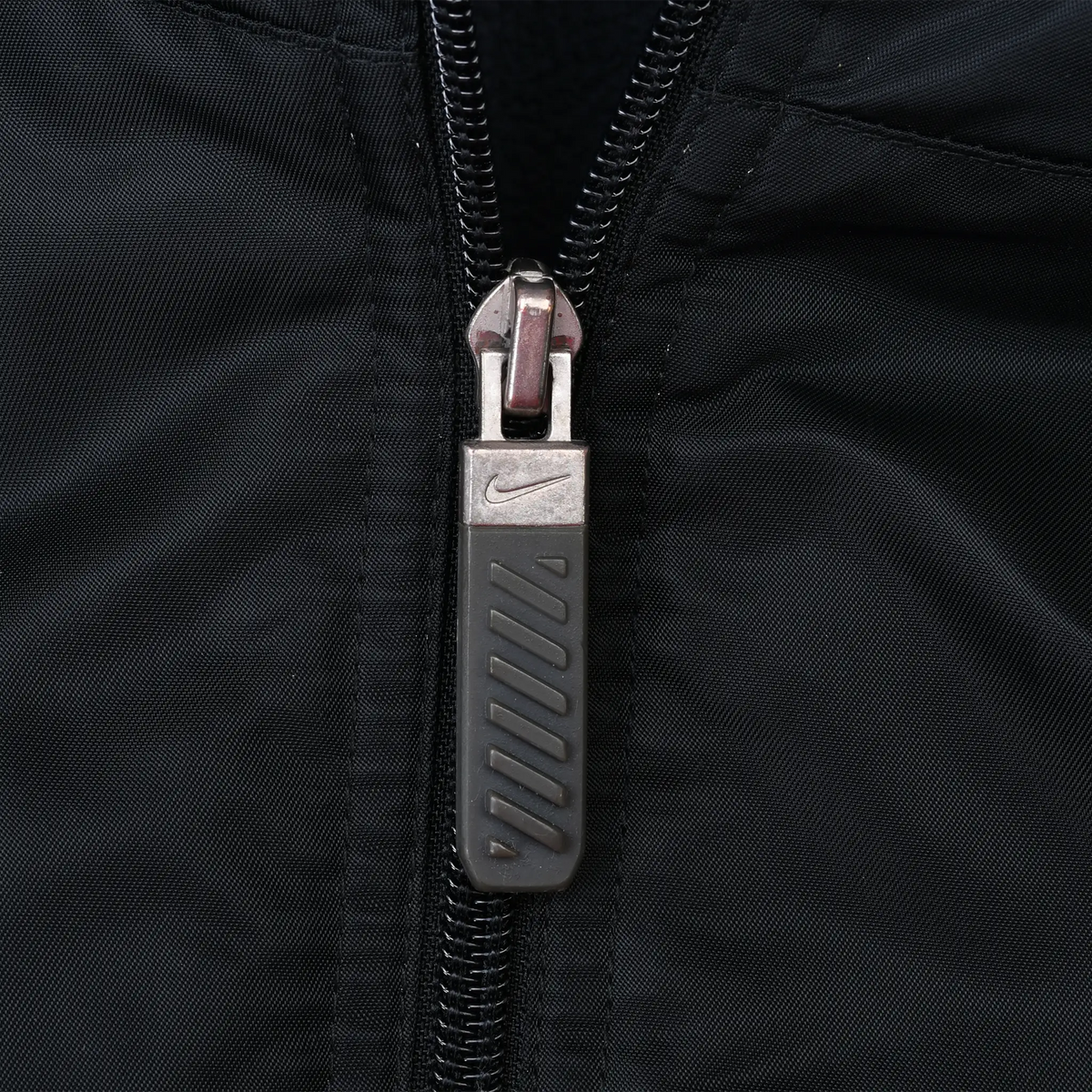 Close-up of Nike Swoosh zipper pull on the black jacket
