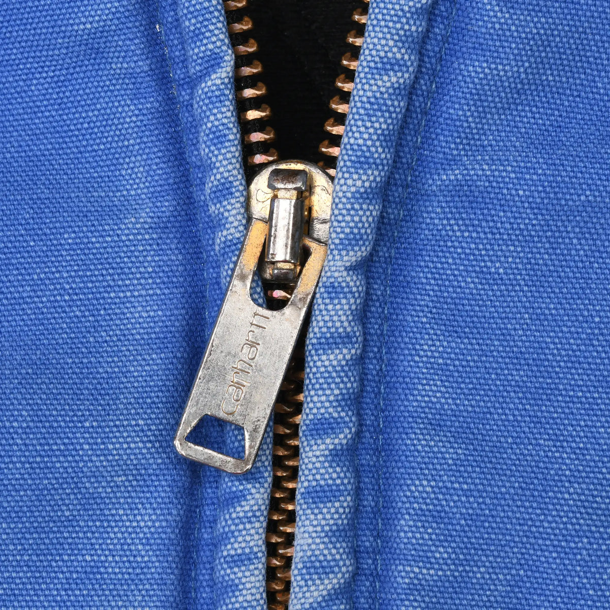 Close-up of Carhartt-engraved metal zipper pull and blue jacket fabric