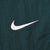 Close-up of small white Nike Swoosh embroidery on green swim trunks